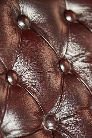 Dark brown leather buttoned background, close-up, shallow depth of field, selective focus. Luxurious...