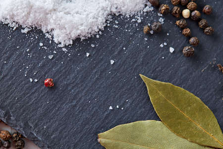 Composition of bay laurel leaf with peppercorn and salt isolated on dark background, top view, close-up, selective focus. Aroma collection culinary herbs and spices. Organic condiment. Food background.の写真素材