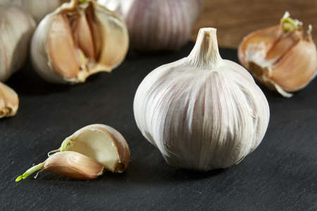 Garlic on flat wooden plate put on rustic rough wooden table with light grey cotton canvas as background. Close-up, shallow depth of field, selective focus, front focus, macro. Healthy lifestyle concept.の写真素材