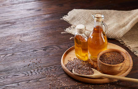 Brown flax seeds in wooden plate and flaxseed oil in glass bottle on brown rustic wooden background, top view, close-up, selective focus. Flax oil is rich in omega-3 fatty acid. Healthy lifestyle concept.の写真素材