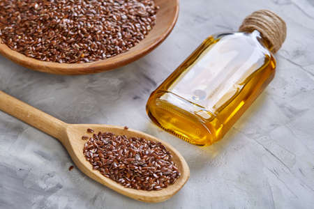 Flax seeds in bowl and flaxseed oil in glass bottle on wooden background, top view, close-up, selective focusの写真素材