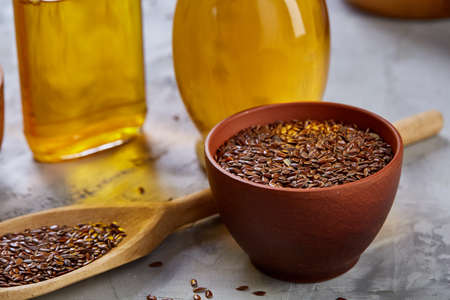 Flax seeds in bowl and flaxseed oil in glass bottle on wooden background, top view, close-up, selective focusの写真素材