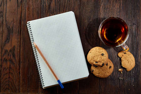 Cup of tea with cookies, workbook and a pencil on a wooden background, top viewの写真素材