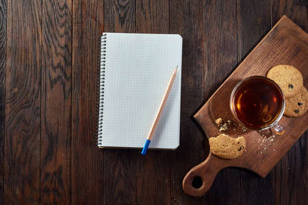 Cup of tea with cookies, workbook and a pencil on a wooden background, top viewの写真素材