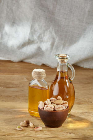 Aromatic oil in a glass jar and bottle with pistacios in bowl on wooden table, close-up, vertical.の写真素材