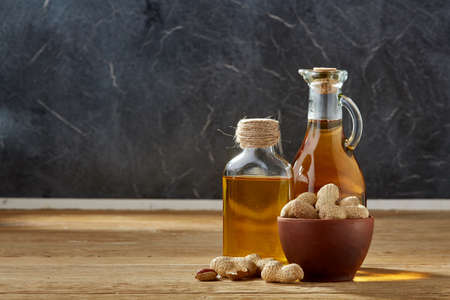 Aromatic oil in a glass jar and bottle with peanuts in bowl on wooden table, close-up.の写真素材