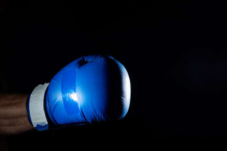 A fighters blue boxing gloves on his hand isolated on dark blurred background, close-up.の写真素材