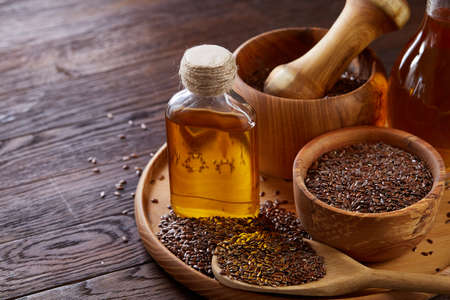 Flax seeds in bowl and flaxseed oil in glass bottle on wooden background, top view, close-up, selective focus.の写真素材