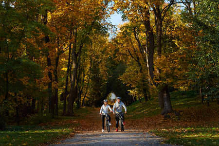 Happy young couple going for a bike ride on an autumn day in the park.の写真素材