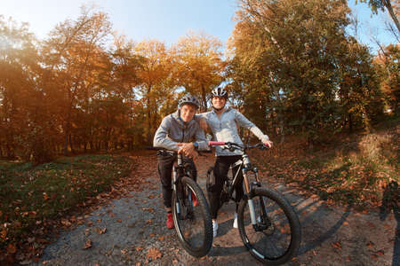 Happy young couple going for a bike ride on an autumn day in the park, backlight.の写真素材