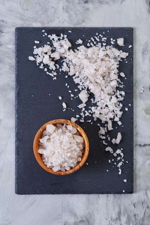 Large white sea salt in a natural wooden bowl on dark board over lifgt background, top view, close-up, selective focusの写真素材