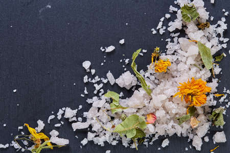 Pile of salt crystals mixed with motley grass on the dark background, close-up, top view, selective focus. Some copy space for your text or inscription. Abstract background. Spa and wellness setting. Spa decoration concept.の写真素材