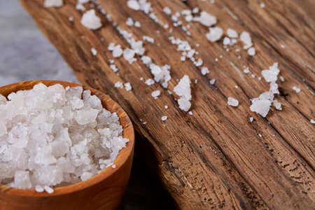 Large white sea salt in a natural wooden bowl on dark background, top view, close-up, selective focusの写真素材