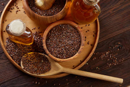 Flax seeds in bowl and flaxseed oil in glass bottle on wooden background, top view, close-up, selective focusの写真素材
