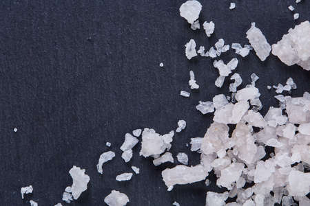 Pile of salt crystals over the dark board on white background, close-up, top view, macro, selective focusの写真素材