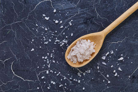 Crystal sea salt in a wooden spoon on dark background, top view, close-up, selective focus.の写真素材