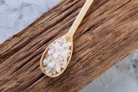 Crystal sea salt in a wooden spoon on dark vintage wooden background, top view, close-up, selective focus.の写真素材