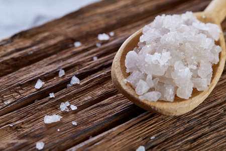 Crystal sea salt in a wooden spoon on dark vintage wooden background, top view, close-up, selective focus.の写真素材