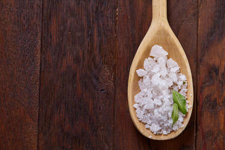 Crystal sea salt in a wooden spoon on dark vintage wooden background, top view, close-up, selective...