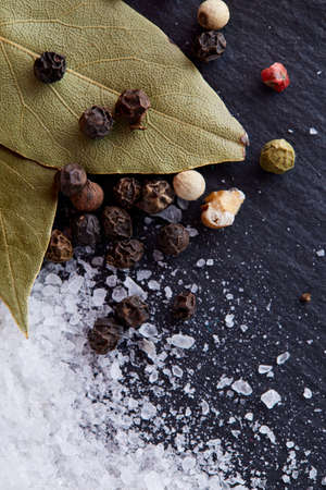 Composition of bay laurel leaf with peppercorn and salt isolated on dark background, top view, close-up, selective focusの写真素材