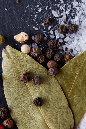 Composition of bay laurel leaf with peppercorn and salt isolated on dark background, top view, close-up, selective focusの写真素材