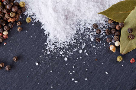 Composition of bay laurel leaf with peppercorn and salt isolated on dark background, top view, close-up, selective focusの写真素材