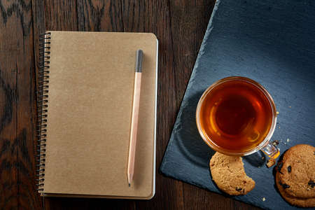 Cup of tea with cookies, workbook and a pencil on a wooden background, top view, verticalの写真素材