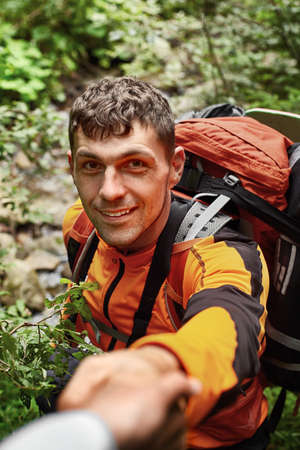 Portrait of happy young man holding hand of his friend while walking by mountain, selective focus.の写真素材