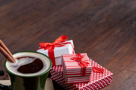Still life with cup of coffee holiday gift in small red color box with ribbon and bow on wooden background, top view, close-upの写真素材