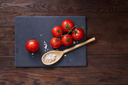 Vegetarian still life with fresh grape tomatoes, pepper and salt in wooden spoon on wooden background, selective focusの写真素材