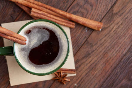 Cup of creamy coffee with cinnamon and star anise on a wooden table, top view, close-up, selective focusの写真素材