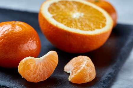 Close-up of whole and half cut fresh tangerine and orange on cutting board over white background, shallow depth of fieldの写真素材