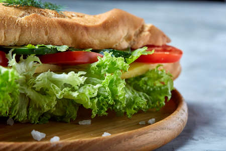Fresh sandwich with lettuce, tomatoes and cheese served on wooden plate over white textured background, selective focusの写真素材