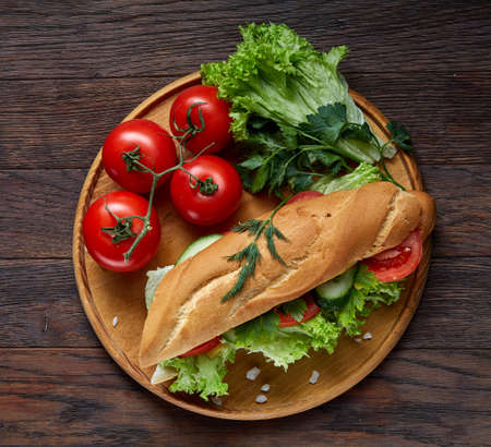 Fresh sandwich with lettuce, tomatoes and cheese served on wooden plate over wooden background, selective focusの写真素材