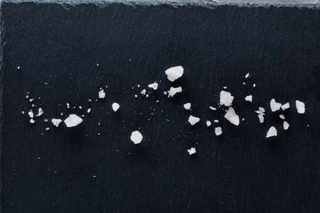 Pile of salt crystals isolated on the dark board over white textured background, close-up,top,view, selective focus. Some copy space for your text or inscription. Abstract background. Spa decoration concept.の写真素材