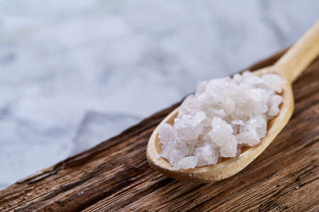 Sea salt crystals in a wooden spoon on dark backgrond, top view, close-up, selective focus, vertical. Some copy space for your inscription. Natural ingredient for your beauty and health. Theurapeutic treatment.の写真素材