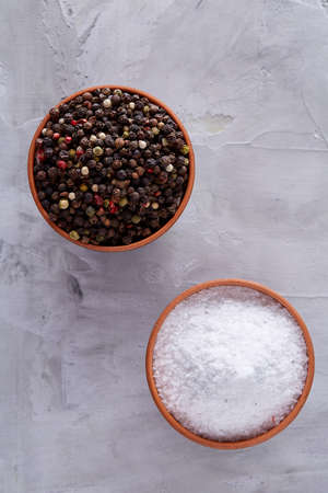 Conceptual composition of salt and pepper on spoons and bowls over light background, top view, close-up. Aromatic and organic condiment. Organic flavour. Cuisine culture. Food background.の写真素材