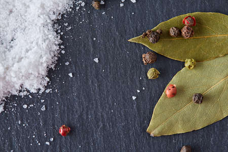 Composition of bay laurel leaf with peppercorn and salt isolated on dark background, top view, close-up, selective focusの写真素材