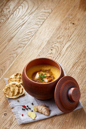 Clay pot of pumpkin soup on homespun napkin rustic wooden background, close-up, selective focus, top view.の写真素材