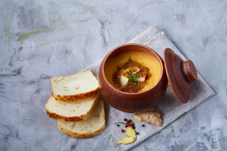 Clay pot of pumpkin soup on napkin over white textured background, close-up, selective focus, top view.の写真素材