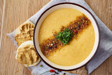 Ceramic bowl of pumpkin soup on napkin over rustic wooden background, close-up, selective focus, top view.の写真素材