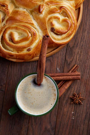 Creamy coffee in cup with homemade rose bread on vintage wooden background, close-up, selective focusの写真素材