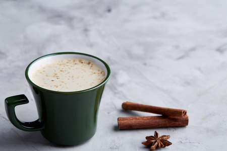 Cup of creamy coffee with cinnamon and star anise on a white textured background, top view,...