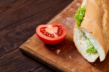 Fresh and tasty sandwich with cheese and vegetables on cutting board over wooden background, selective focus.の写真素材