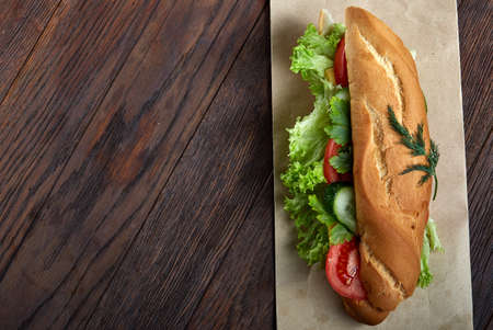 Fresh sandwich with lettuce, tomatoes, cheese on wooden plate, cup of coffee on rustic background,...