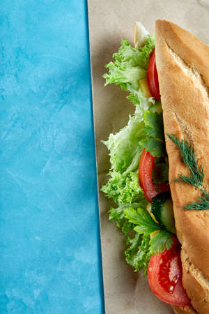 Fresh and tasty sandwich with cheese and vegetables on paper plate over blue background, selective focus, top viewの写真素材