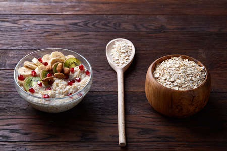 Composition with bowl of oatmeal porrige and dry oatmeal in wooden bowl on vintage background,...