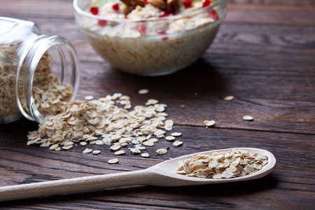 Composition with bowl of oatmeal porrige and dry oatmeal in glassware on vintage wooden table,...