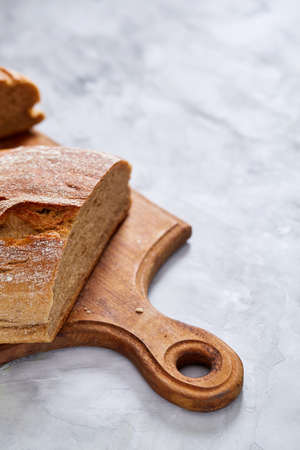 Fresh rye bread loaf on a wooden chopping board over white textured background, shallow depth of...