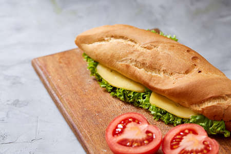 Fresh and tasty sandwich with cheese and vegetables on cutting board over white textured background, selective focus.の写真素材